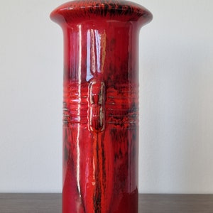 May include: A red ceramic vase with black glaze accents. The vase has a wide, rounded top and a cylindrical body.