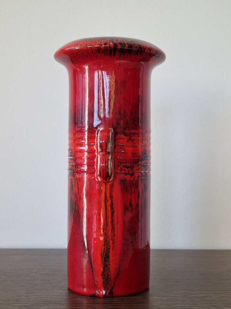 May include: A red ceramic vase with black glaze accents. The vase has a wide, rounded top and a cylindrical body.