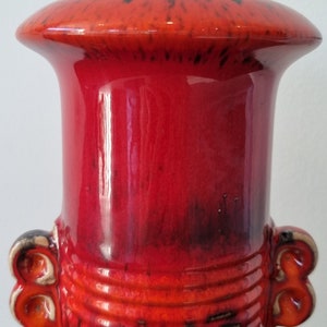 May include: A red and black ceramic vase with a wide mouth and two handles. The vase has a textured surface and a glossy finish.