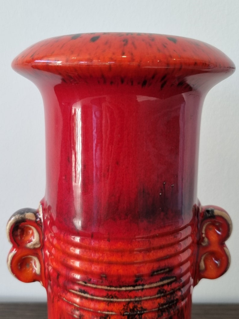 May include: A red and black ceramic vase with a wide mouth and two handles. The vase has a textured surface and a glossy finish.