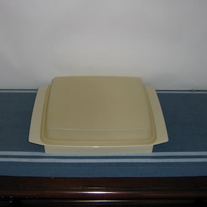 May include: A beige square food storage container with a matching lid. The container has a slightly raised edge and a flat top. The lid fits snugly on top, creating an airtight seal. The container is made of durable plastic.