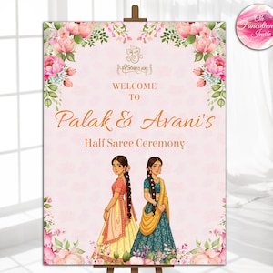 Pode incluir: Uma placa de boas-vindas de casamento rosa em um cavalete, com detalhes florais. A placa diz "Welcome to Palak & Avani's Half Saree Ceremony". Duas mulheres ilustradas em trajes tradicionais na parte inferior.
