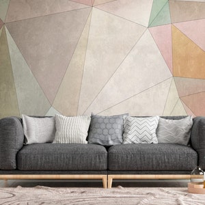 Può includere: Un divano grigio con diversi cuscini in un soggiorno con una parete a motivi geometrici in tonalità di rosa, verde e beige.