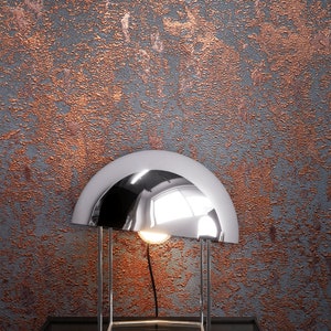 Peut inclure: Une lampe de table chrom&eacute;e avec un abat-jour en forme de d&ocirc;me repose sur une table noire contre un mur textur&eacute; de couleur cuivre.