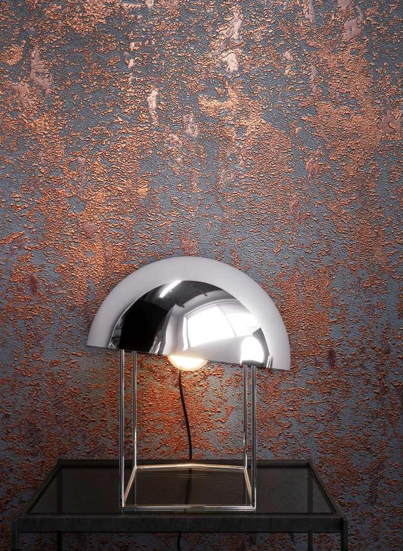 Peut inclure: Une lampe de table chrom&eacute;e avec un abat-jour en forme de d&ocirc;me repose sur une table noire contre un mur textur&eacute; de couleur cuivre.