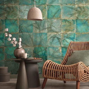 Op de afbeelding: Een rieten stoel met een groen kussen staat in een kamer met een groene en bruine betegelde muur. Een geweven hanglamp hangt boven een bijzettafel met een vaas met katoenen bloemen en een kopje en schoteltje.