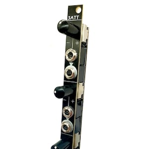 May include: A black and silver electronic module with the text "3ATT" printed on it. The module has three knobs and three sets of jacks with plus and minus signs.