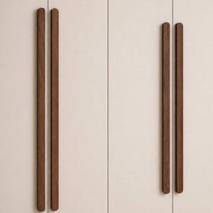 Op de afbeelding: Vier lange, verticale kastgrepen van donkerbruin hout met afgeronde uiteinden. De grepen zijn in twee paren gemonteerd op een glad, lichtbeige oppervlak en hebben een recht, slank ontwerp dat parallel loopt aan de verticale paneelnaden.