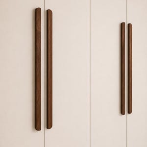 Può includere: Primo piano di un armadio color crema con due set di maniglie in legno marrone scuro. Le maniglie sono lunghe, rettangolari e orientate verticalmente, offrendo un'estetica minimalista. Le ante dell'armadio sono lisce.
