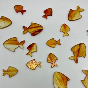 May include: A collection of 15 small, orange and yellow glass fish with a marbled pattern. The fish are scattered on a white background.