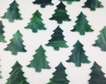 May include: A collection of multiple small, flat, tree-shaped cutouts made of variegated green glass. Each piece features a distinct marbled pattern with swirls of dark and light green tones, shaped like stylized evergreen trees with pointed tops.