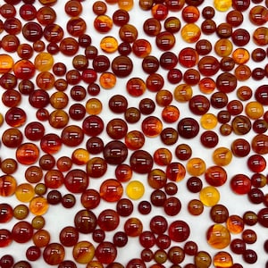 May include: A collection of round, translucent cabochons in shades of red, orange, and yellow. The cabochons are scattered on a white surface.