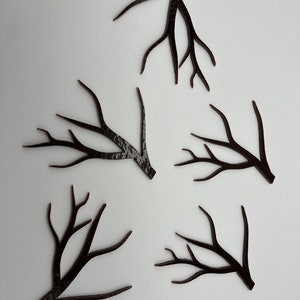 May include: Five black paper cutouts of tree branches with varying shapes and sizes. The branches are arranged in a random pattern on a white background.