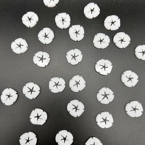 May include: A collection of white plastic star-shaped buttons with a hole in the center. The buttons are arranged in a circular pattern on a black surface.