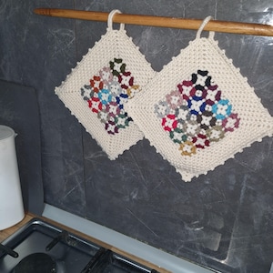 Peut inclure: Deux dessous de plat carrés en tricot blanc cassé avec des motifs floraux colorés. Chaque dessous de plat a une boucle pour être suspendu et est suspendu à une tige en bois. Les motifs floraux présentent diverses couleurs, dont le rouge, le bleu et le vert.
