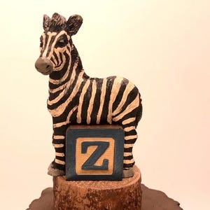 May include: A black and white zebra figurine standing on a wooden base with a blue and brown block that says "Z" on it.