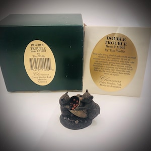 May include: A dark brown bear cub figurine titled Double Trouble by Tim Wolfe, featuring two cubs reaching into a wooden barrel filled with red apples. The set includes a dark green box and a white informational card with gold oval text.