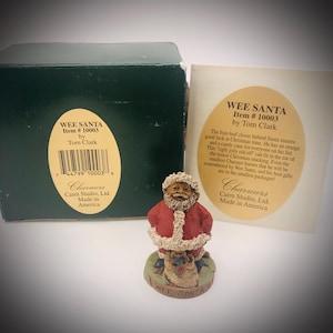 May include: A Wee Santa figurine by Tom Clark, item number 10003, featuring a bearded Santa in a red suit with white trim, standing on a base labelled Wee Santa. The set includes a dark green box and a descriptive card with the text Wee Santa.