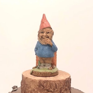 May include: A small, hand-painted gnome figurine with a red hat, blue shirt, and a mischievous grin. The gnome is sitting on a wooden stump with the words "Widecracker" inscribed on the base.