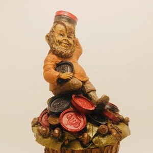 May include: A whimsical figurine of a gnome wearing a red hat and holding a chocolate chip cookie. The gnome is sitting on a pile of chocolate chip cookies and red poker chips.