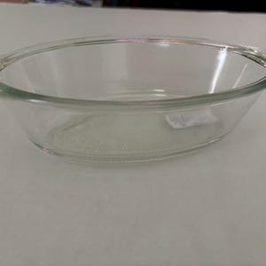 May include: A clear, oval-shaped glass bowl with a rounded rim. The bowl is transparent, allowing a view of the contents. The design is simple and functional, suitable for serving or food preparation.