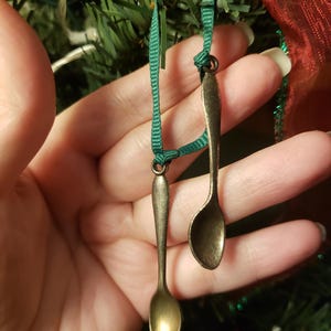 May include: Two small, antique-looking spoons with green ribbon hanging from a Christmas tree.