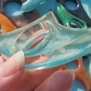 May include: A translucent blue resin ring with a unique, abstract shape and a sparkly finish.