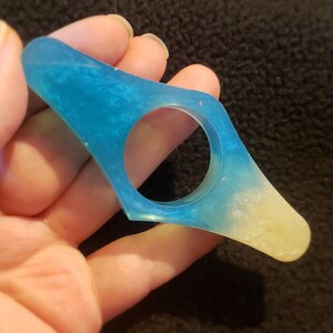 May include: A blue and white glitter bookmark with a rounded shape. The bookmark is made of resin and has a glittery finish.