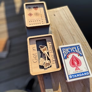 May include: Wooden framed game pieces with the text "Get in the Barn!" and a deck of Bicycle playing cards. The game pieces feature a cow, overalls, and a guitar. The playing cards have a red spade design.