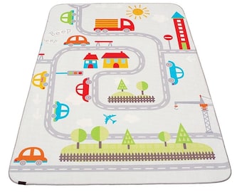 Puede incluir: Una alfombra de juego blanca con una escena de carretera y ciudad. La alfombra presenta un camión, coches, casas, árboles, una grúa, un semáforo y una señal de stop. El texto "Beep" está escrito en la alfombra.