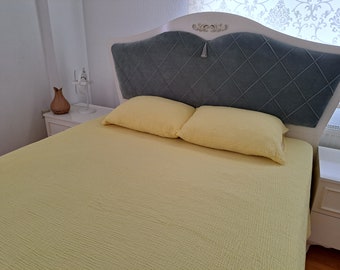 May include: A yellow bedspread with two yellow pillows on a white bed frame with a grey headboard. The headboard has a diamond pattern and a tassel.