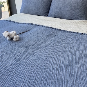 May include: A blue waffle weave throw blanket with a white cotton flower on top. The blanket has a frayed edge.