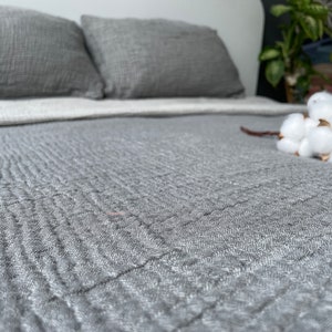 May include: A gray quilted bedspread with a white cotton flower arrangement on top.