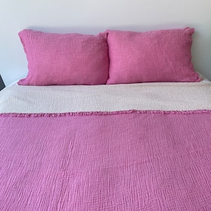 May include: A pink and white quilt with a fringed edge. The quilt is made of a soft, textured fabric and is perfect for adding a touch of colour and comfort to any bedroom.