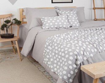 Può includere: Un letto grigio con biancheria da letto e cuscini a pois bianchi. Il letto è fatto con una federa grigia e una coperta a pois bianchi. Il letto è in una camera da letto con una parete bianca e grigia e una scala di legno.