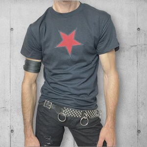 A black t-shirt with a red star on the front. The t-shirt is being worn by a person with a black leather bracelet on their left wrist and a studded black belt with silver rings.