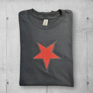 A black t-shirt with a red star design on the front. The star is outlined in black and has a slightly distressed look.