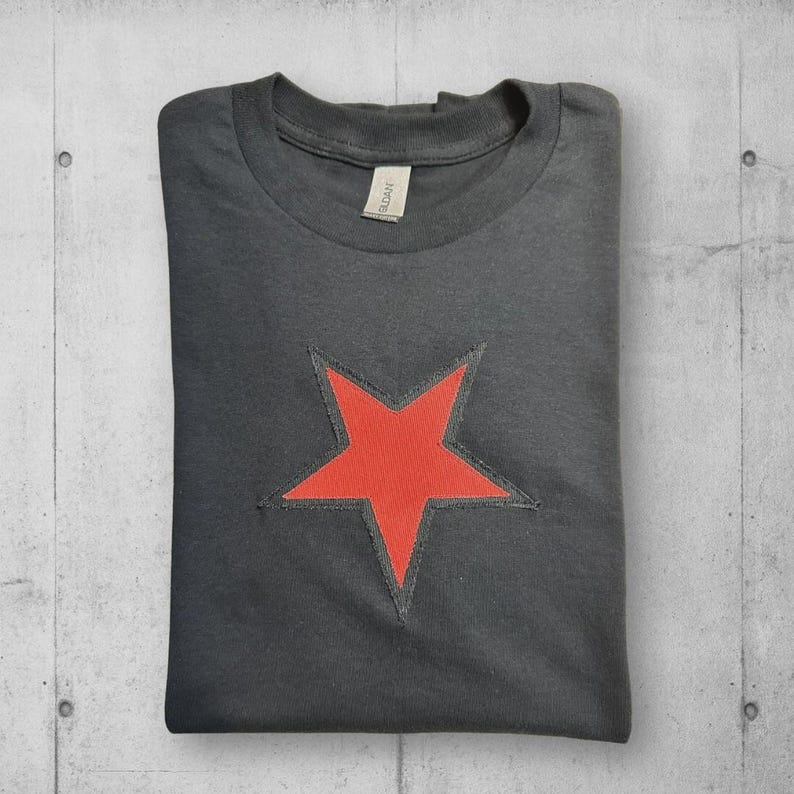 A black t-shirt with a red star design on the front. The star is outlined in black and has a slightly distressed look.