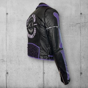 May include: Black faux leather jacket with purple accents, studs, and bone design on the sleeve. The back features a skull graphic with the text "ALWAYS FOLLOW SOMEONES STORY". The jacket has a zipper closure and a classic biker style.