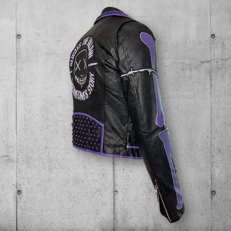 May include: Black faux leather jacket with purple accents, studs, and bone design on the sleeve. The back features a skull graphic with the text "ALWAYS FOLLOW SOMEONES STORY". The jacket has a zipper closure and a classic biker style.