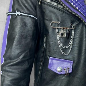 May include: Black leather jacket with purple accents, a silver chain, and a safety pin. The jacket features a barbed wire patch, a purple pocket, and a zipper closure. The collar is adorned with purple studs.
