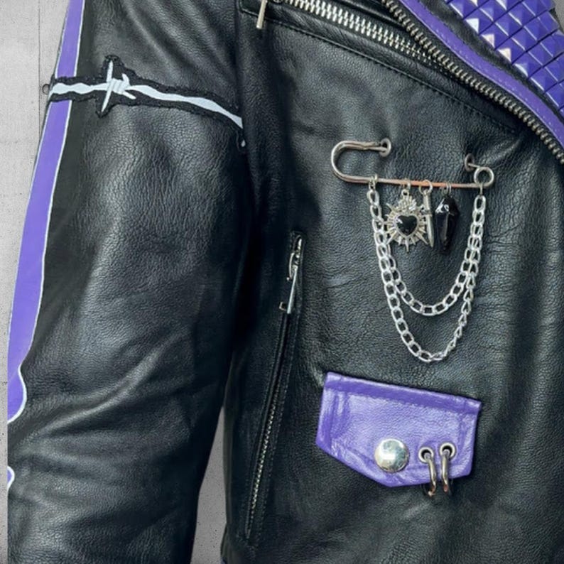 May include: Black leather jacket with purple accents, a silver chain, and a safety pin. The jacket features a barbed wire patch, a purple pocket, and a zipper closure. The collar is adorned with purple studs.