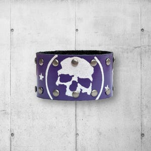 May include: Purple leather bracelet with a white skull design and silver studs.