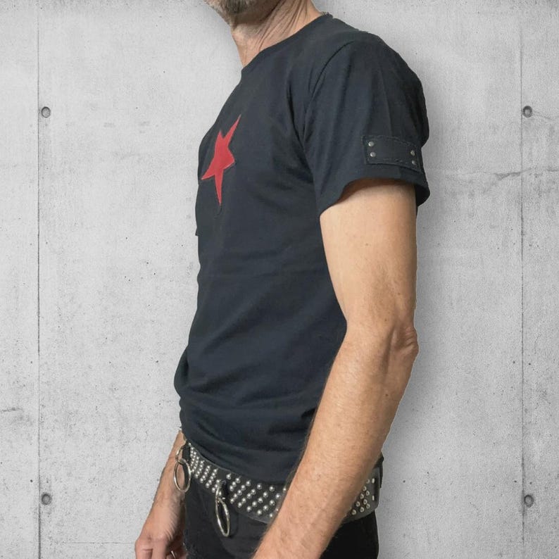 A black t-shirt with a red star on the front and a black denim patch on the sleeve. The t-shirt is worn with a black studded belt.
