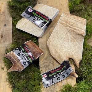 May include: Three different sizes of natural fallow deer antlers for dogs. The antlers are light brown and have a rough texture. The packaging says "100% Natural Fallow Deer Antler Dog Chew".