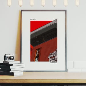 Può includere: Una stampa incorniciata di un'illustrazione rossa e grigia dell'Anfield Stadium, casa del Liverpool Football Club. La stampa include il testo "Anfield" e lo stemma del Liverpool con le parole "You'll Never Walk Alone" e "Liverpool".