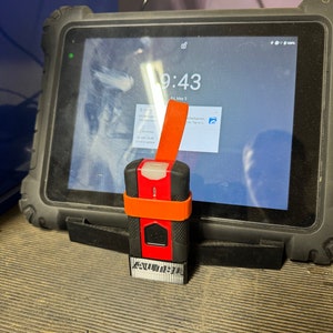 Może przedstawiać: Czerwono-czarne urządzenie z pomarańczowym paskiem, oznaczone jako "NUM DATA", jest przymocowane do czarnego tabletu z ekranem wyświetlającym godzinę "9:43" i datę "Fri, May 3".