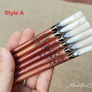 Puede incluir: Un juego de seis palillos personalizados con un dise&ntilde;o de m&aacute;rmol blanco y negro. Los palillos est&aacute;n hechos de madera y tienen un revestimiento de resina epoxi transparente. Los nombres "Akirami", "Tyler", "タイラー", "기록원", y "기록원" est&aacute;n grabados en los palillos.