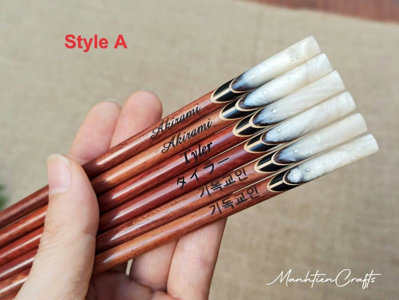 Puede incluir: Un juego de seis palillos personalizados con un dise&ntilde;o de m&aacute;rmol blanco y negro. Los palillos est&aacute;n hechos de madera y tienen un revestimiento de resina epoxi transparente. Los nombres "Akirami", "Tyler", "タイラー", "기록원", y "기록원" est&aacute;n grabados en los palillos.