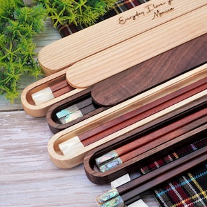 May include: A collection of wooden chopstick sets in sliding cases. The top case is light wood with the engraved text "Everyday I love you more! Monica". Other cases are dark wood, containing chopsticks with iridescent shell inlays.